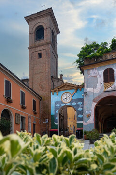 Bologna, Italy - 26 March 2022: View of the vibrant colors of the archway and the imposing bell tower reaching towards the sky, framed by the lush greenery of the foreground.