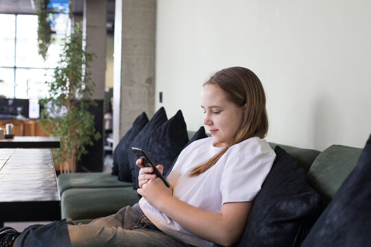 Cheerful preteen child holding mobile cell phone. Girl playing games with apps and checking social media indoor