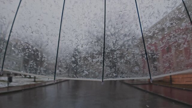 POV video, sleet falling on a transparent umbrella during a walk in the park in the historical center of the European city, slow motion