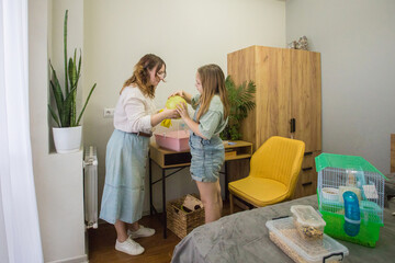 Naklejka premium Mom and daughter are working together to set up a pet enclosure in a bedroom. One girl holds a yellow item above her head while the other watches closely.