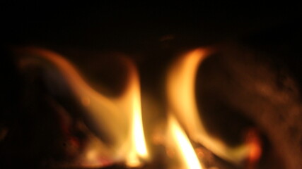 Fototapeta premium Wooden logs are burning in the fireplace. Tongues of flame on a dark background. 