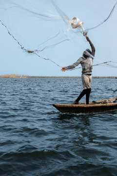 Ganvie, Benin - 14 April 2023: View of a fisherman casting his net from a small boat, creating a dynamic contrast against the deep blue water and clear sky.