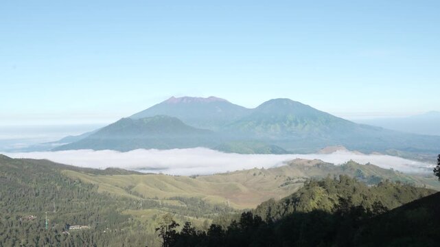 Wide view of Mount Raung volcano with morning mist over green valleys in Indonesia