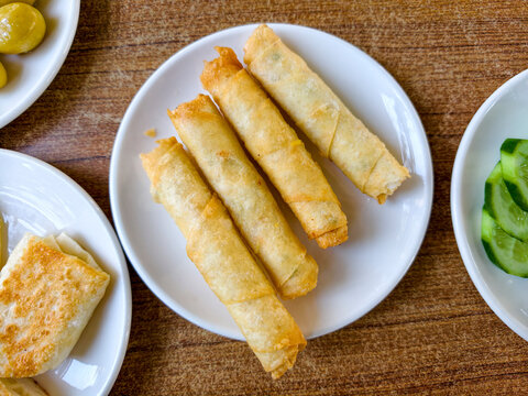 Golden spring rolls served on a white plate next to flatbread and cucumbers in a casual dining setting