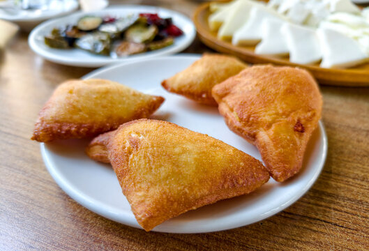 Warm pastry filled with savory ingredients served on a white plate alongside various side dishes in a casual dining setting
