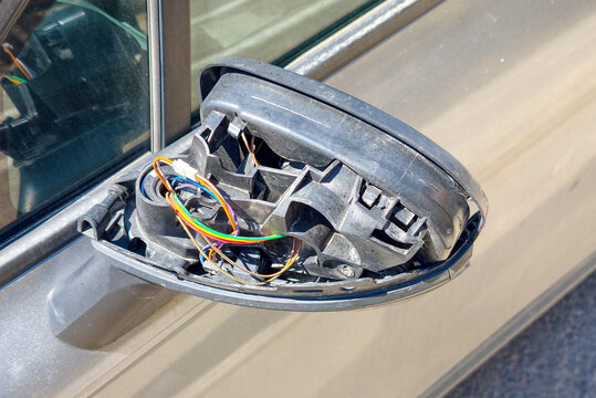 Broken side mirror with exposed wiring on a parked car in an urban area during daylight hours