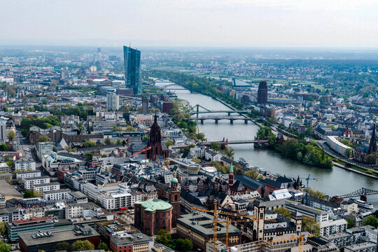 View of the Main River snaking through the urban sprawl, bridges connecting the vibrant cityscape under a hazy sky, blending old and new architecture, Frankfurt am Main, Hessen, Germany.