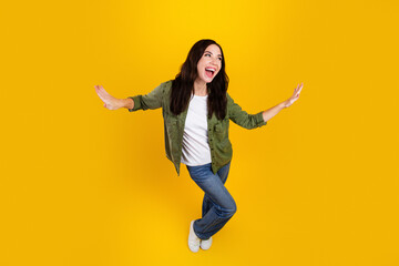 Happy young woman balancing playfully on one foot against a bright yellow background, expressing...