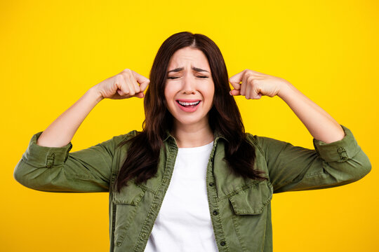 Young woman plugging her ears and wincing in frustration against a bright yellow background