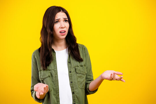 Confused young woman shrugging with puzzled expression against bright yellow background, casual portrait showing uncertainty and frustration