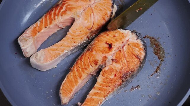 Close-up of salmon steaks frying in a pan as a chef flips them with a spatula. The footage captures the cooking process, texture, and movement, highlighting healthy seafood and professional food