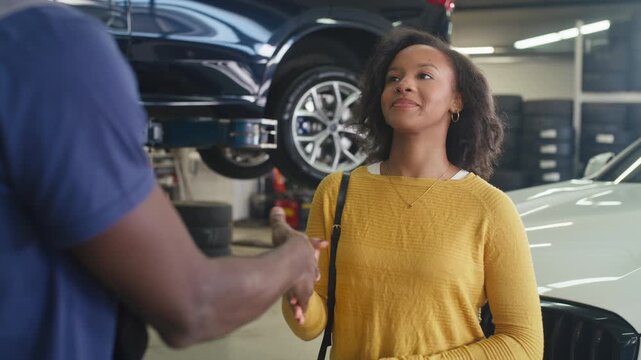 Professional service and customer satisfaction in an auto repair shop, a mechanic shaking hands and returning the car keys to a smiling owner.