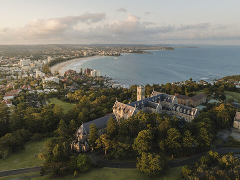 Aerial view of St Patrick's Seminary casting a long shadow over the lush green landscape, with the beach and ocean beyond, Manly, New South Wales, Australia.