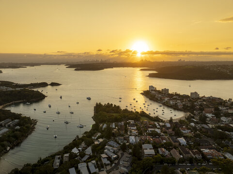 Aerial view of a tranquil bay, dotted with boats, ablaze in the golden light of sunset, contrasting with the dark land, Manly, New South Wales, Australia.