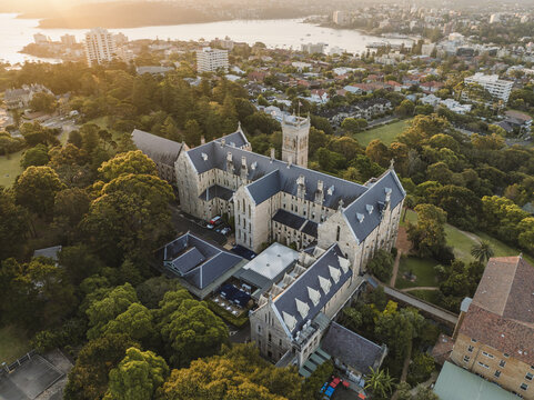 Aerial view of St Patrick's Seminary bathed in the golden light of dawn, nestled amongst lush greenery with a serene bay backdrop, Manly, New South Wales, Australia.