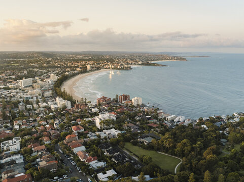 Aerial view of Manly's golden crescent beach meeting the deep blue ocean, framed by a coastal town and verdant parkland, Manly, New South Wales, Australia.