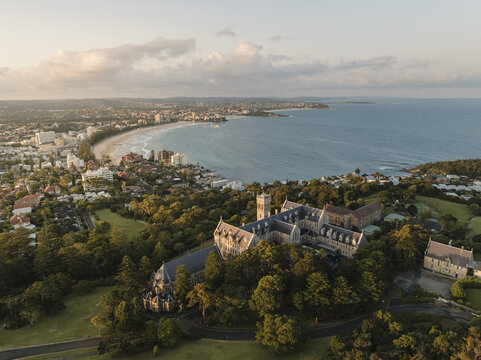 Aerial view of the majestic St Patrick's Seminary amidst a sea of green trees, overlooking the golden sands of Manly Beach, Manly, New South Wales, Australia.