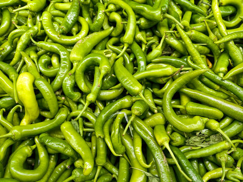Bright green chilies are piled together in a market setting during the day