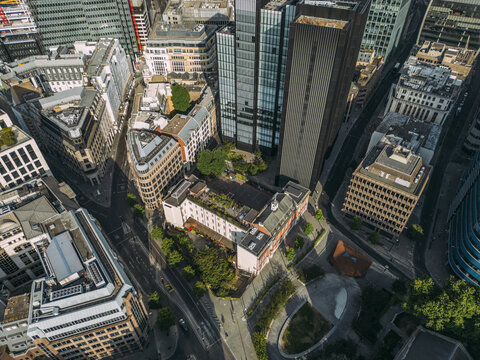 Aerial view of soaring glass towers contrasting with traditional buildings and green rooftops, woven by city streets, City of London, London, United Kingdom.