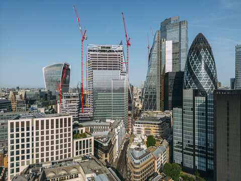 Aerial view of iconic skyscrapers like The Gherkin and Walkie-Talkie rising above the historic streets, bathed in bright sunlight, City of London, London, United Kingdom.