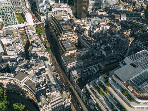 Aerial view of a vibrant cityscape blending historic architecture with gleaming modern structures and lush rooftop gardens under a bright sky, City of London, London, United Kingdom.