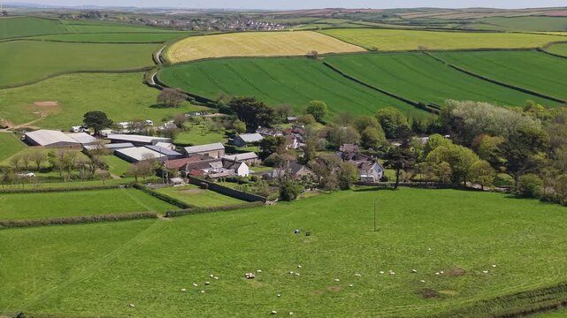Aerial drone footage of Putsborough village in North Devon, England, showcasing a peaceful rural setting near the coast with green fields, rolling hills, and traditional houses under a sunny sky