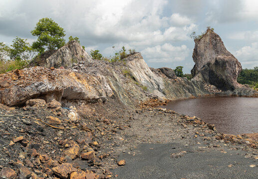 The Sculpted Silence of Nong Bua Under a sprawling canopy of pale, heavy clouds, the landscape reveals a rugged arena of industrial archaeology. A massive, monolithic pillar of weathered rock stands a