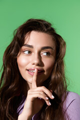 Naklejka premium Stylish woman playfully holding a finger to her lips against a vibrant green backdrop