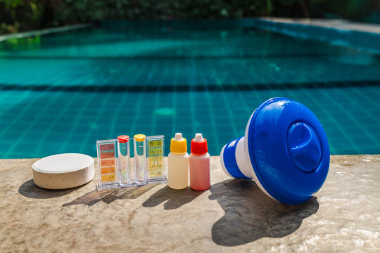 Pool water testing kit, chemical reagent bottles, chlorine tablet, and floating dispenser on pool edge for swimming pool maintenance and water quality control
