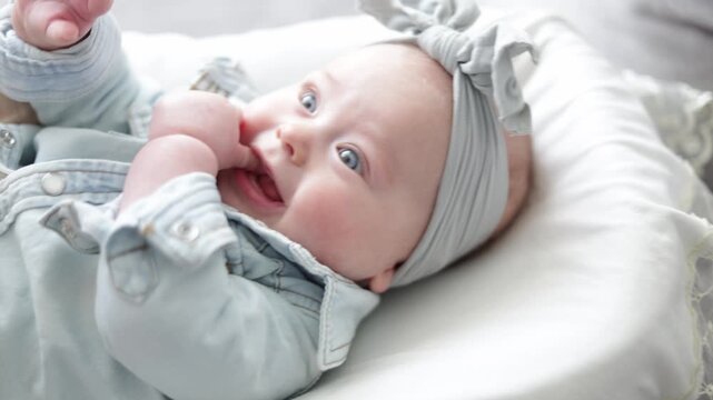 Adorable baby girl with blue eyes and a bow on her head sucks her thumb