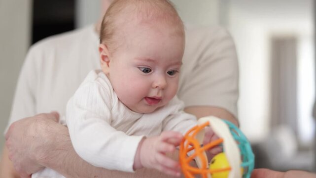Father holding baby and playing with colorful rattle toy indoors