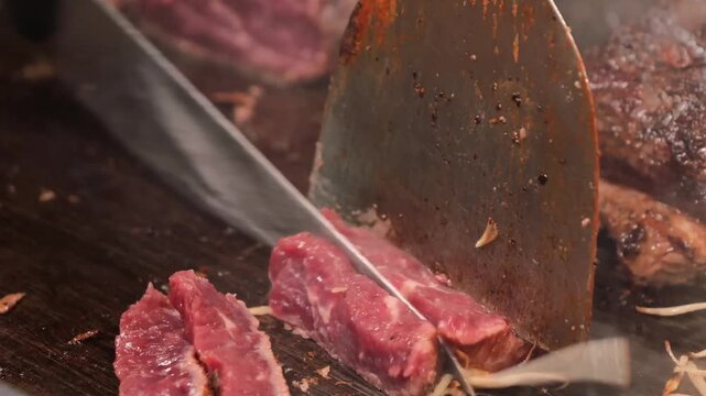 A close-up shot of a professional teppanyaki chef using a sharp carving knife to slice into a juicy, medium-rare Wagyu beef steak on a hot iron griddle. The scene captures rising steam and the meticul