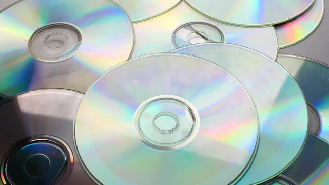 close-up hand throwing compact disc onto pile of CDs, reflective surfaces and motion create dynamic and modern scene. Ideal for technology concepts, data storage themes, retro media visuals