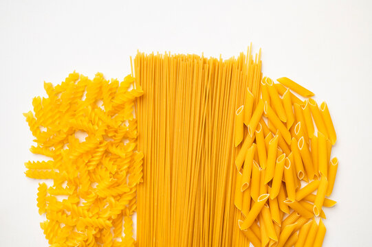 Dry uncooked Italian pasta scattered on white background, top view space for text. Spiral pasta, fusilli, penne, spaghetti. Food background, organic macaroni made from wheat flour
