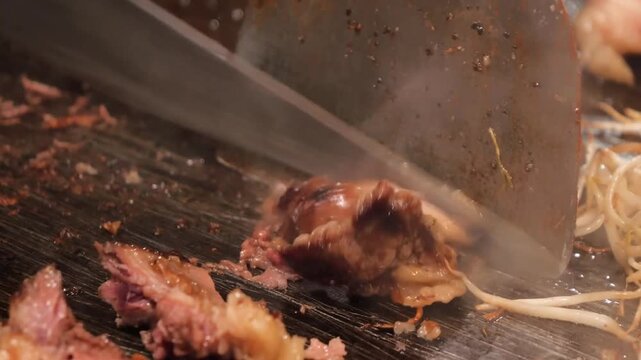 A professional chef uses a metal spatula to flip and sear a thick, juicy cut of premium Wagyu beef on a steaming hot teppanyaki grill. The footage captures the sizzling texture and rich marbling of th