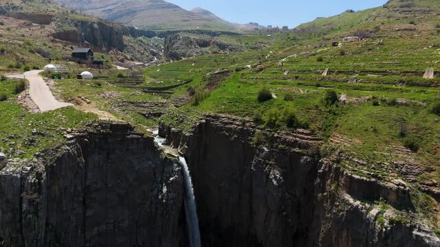 High angle drone shot showing waterfall in Faraya surrounded by mountains and green land during daytime