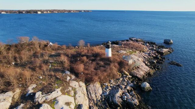 Historic Annisquam Harbor Lighthouse on rocky peninsula at sunset in Gloucester, Massachusetts, USA. Aerial drone orbiting