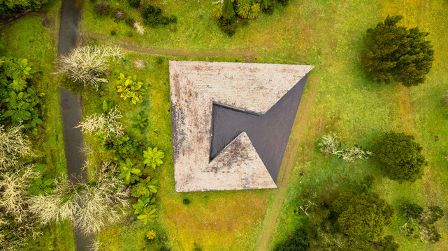 Aerial view of an angular, light-toned structure nestled amidst a tapestry of vibrant green and golden foliage, Ponta Delgada, Azores, Portugal.