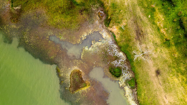 Aerial view of emerald waters contrasting with a textured shoreline of brown marsh, white geothermal deposits, and green land, Ponta Delgada, Azores, Portugal.