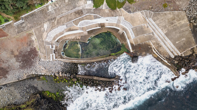 Aerial view of the tranquil, moss-covered pools cascade down to meet the ocean's crashing waves, a stark contrast of textures and tones, Ponta Delgada, Azores, Portugal.