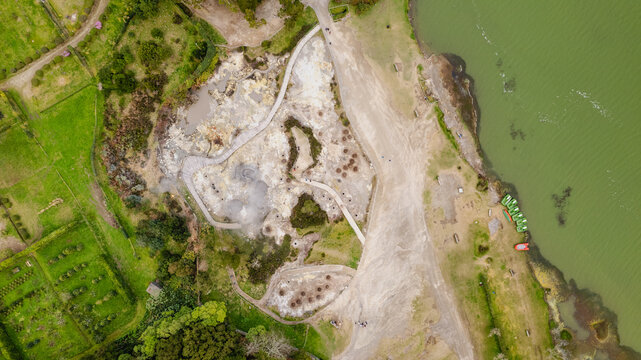 Aerial view of steaming geothermal mud pots contrasting lush green fields and a dark lake, Ponta Delgada, Azores, Portugal.