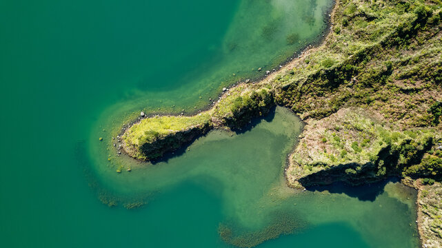 Aerial view of vibrant green waters meeting a rugged, dark landmass with intricate shoreline textures, Ponta Delgada, Azores, Portugal.