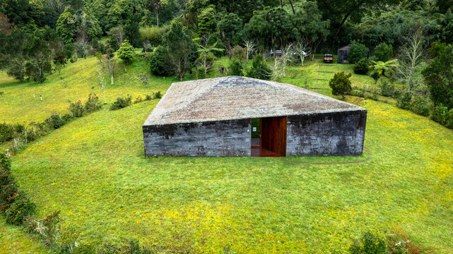 Aerial view of a dark, angular building on a vibrant green hill, framed by lush forest, Ponta Delgada, Azores, Portugal.