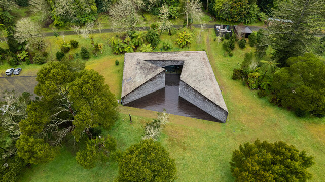 Aerial view of a striking angular dark stone structure, its sharp lines contrasting with the lush emerald landscape, Ponta Delgada, Azores, Portugal.