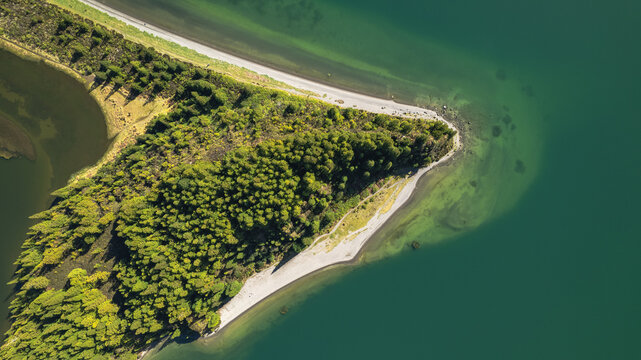 Aerial view of a vibrant green forested peninsula sharply contrasting with the deep emerald waters and a pale sandy beach, Ponta Delgada, Azores, Portugal.