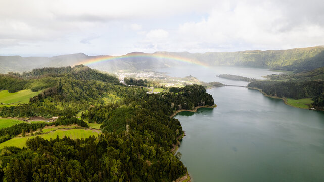 Aerial view of a rainbow over the serene Sete Cidades twin lakes, framed by lush emerald forests, Ponta Delgada, Azores, Portugal.