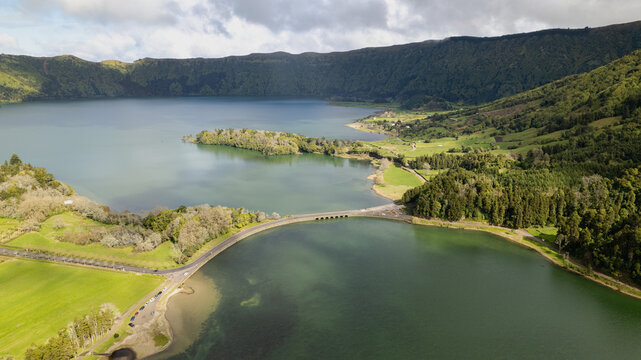 Aerial view of a stunning lake surrounded by verdant hills and lush green fields, divided by a narrow isthmus, Ponta Delgada, Azores, Portugal.