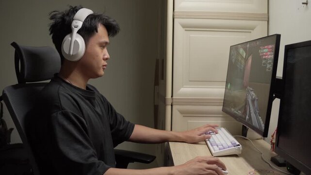 Young man focused on playing first-person shooter video game at home desk setup