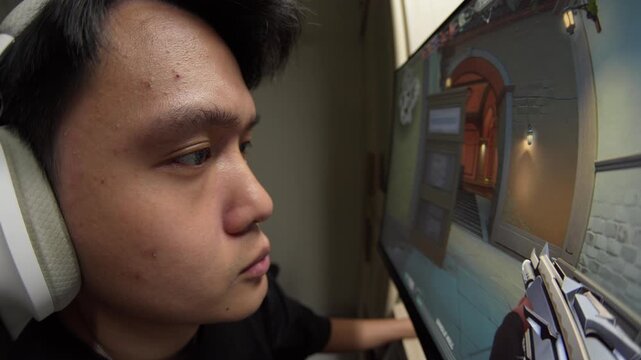 Focused gamer wearing headphones plays first-person shooter on desktop monitor