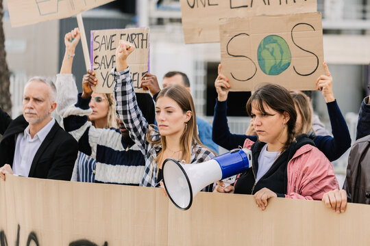 Group of activists demonstrating for environmental protection and climate action, holding protest signs with slogans like save earth and an sos symbol, showing solidarity